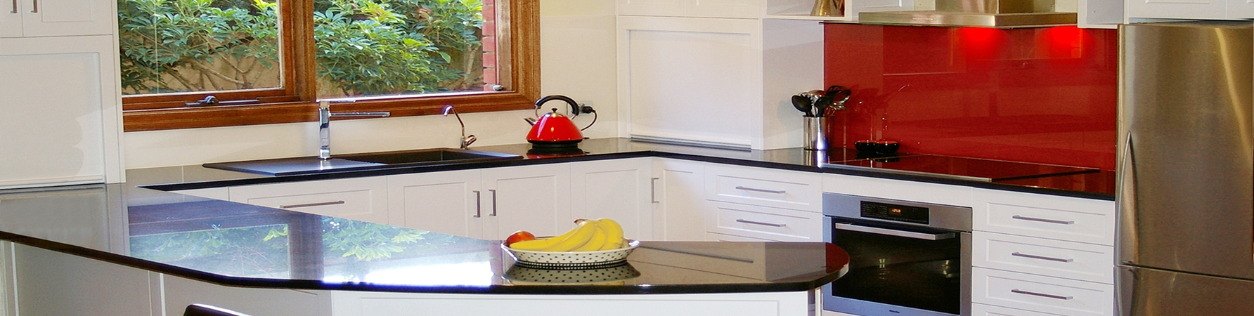 Modern white kitchen with black benchtops and red glass splashback